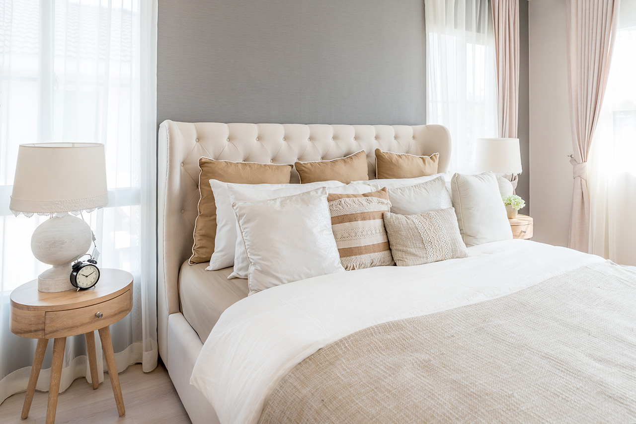 Bedroom in soft light colors. Big comfortable double bed in elegant classic bedroom